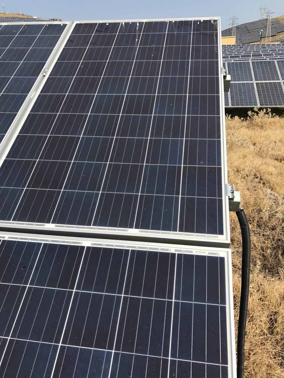 Panel kenarındaki bağlantı kutusundan çıkan kablonun kuru otların arasına uzandığı görünüm