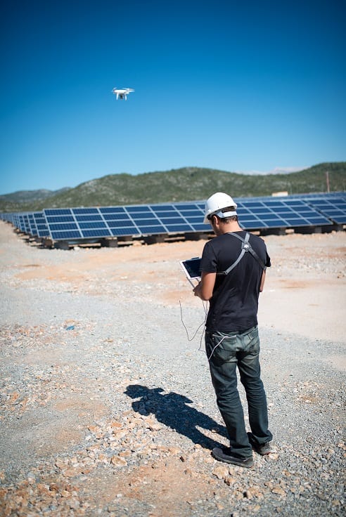 Teknisyen tabletle drone uçuşunu yönetiyor, arka planda güneş paneli dizileri